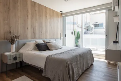 Dormitorio moderno con pared de madera y cama gris — proyecto Depto Arribeños, por Ayelen Mayer Arquitectura, en Buenos Aires